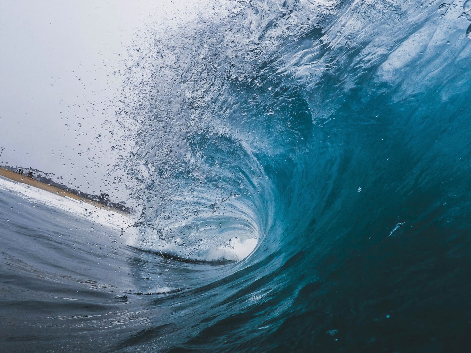 A wave in Newport Beach, USA The barrel of a crystal blue wave crashing down towards the shore, with the crest spraying water.